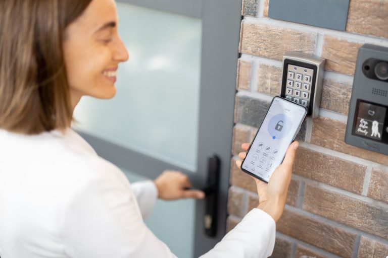 A woman looks at a door lock, smartphone in hand, assessing the security feature with concentration.