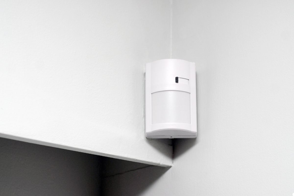 A white wall-mounted alarm is positioned in the corner of a room, blending with the wall's surface.
