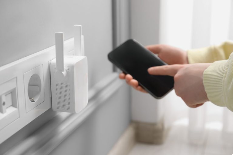 A person holds a cell phone near a wall outlet, demonstrating the connection between the device and power source.