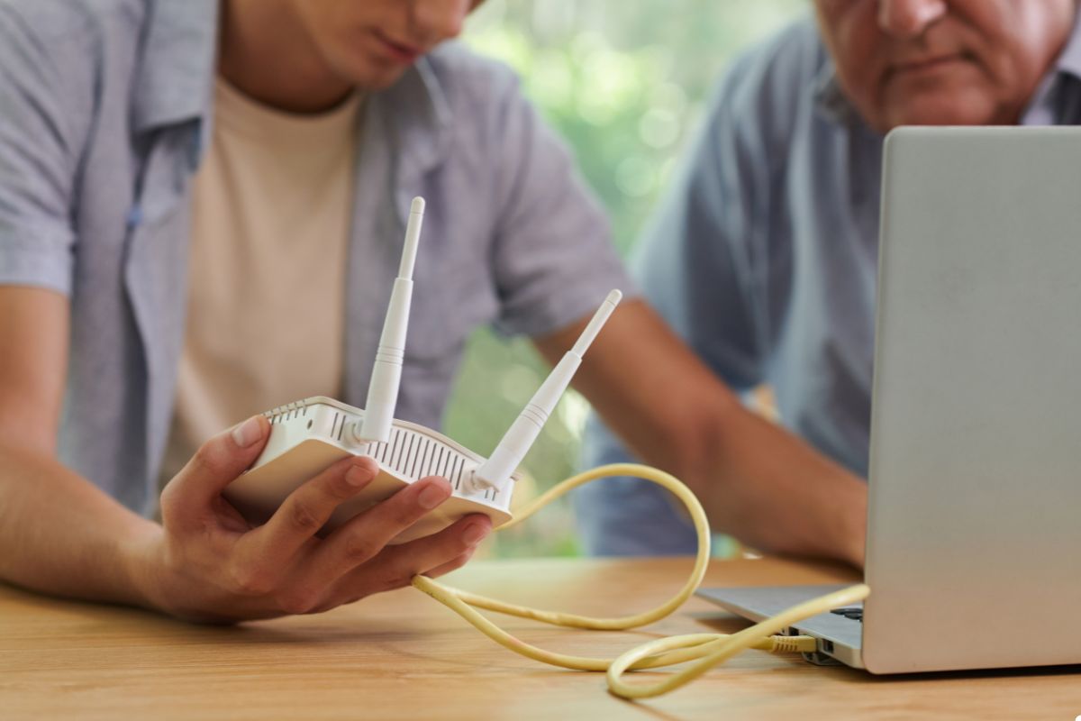 Two men focused on a laptop, with a router nearby, indicating a collaborative work environment.